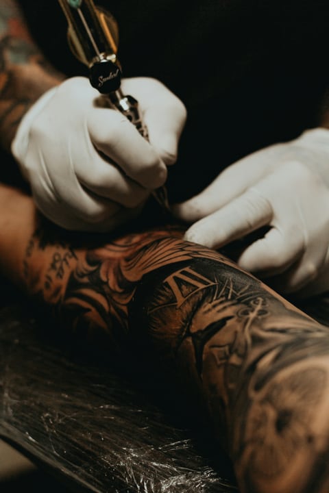 Tattoo artist in black gloves working on a client's sleeve tattoo